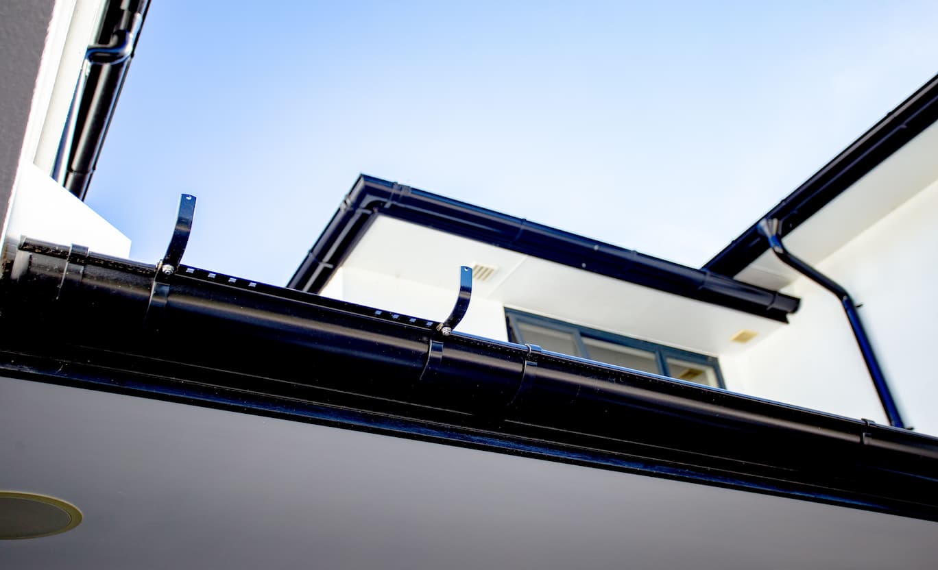 Black Lindab guttering with a Ladder Bracket attached to a building's side.