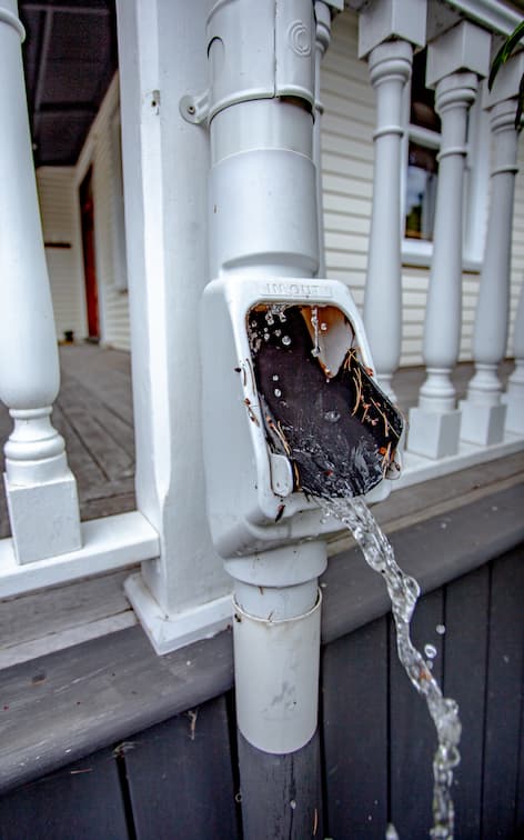 A downpipe attached to a deck with a In/Out Debris Diverter with water flowing out