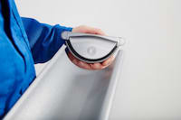 A man in a blue jacket holds a metal tray showcasing self-sealing stop ends with high-quality EPDM tubing, easily mounted and reversible with a firm knock.