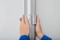 A person holds a metal pole with a downpipe holder. Our sheet steel pipe holder ensures easy installation, no lost accessories or askew mounting.